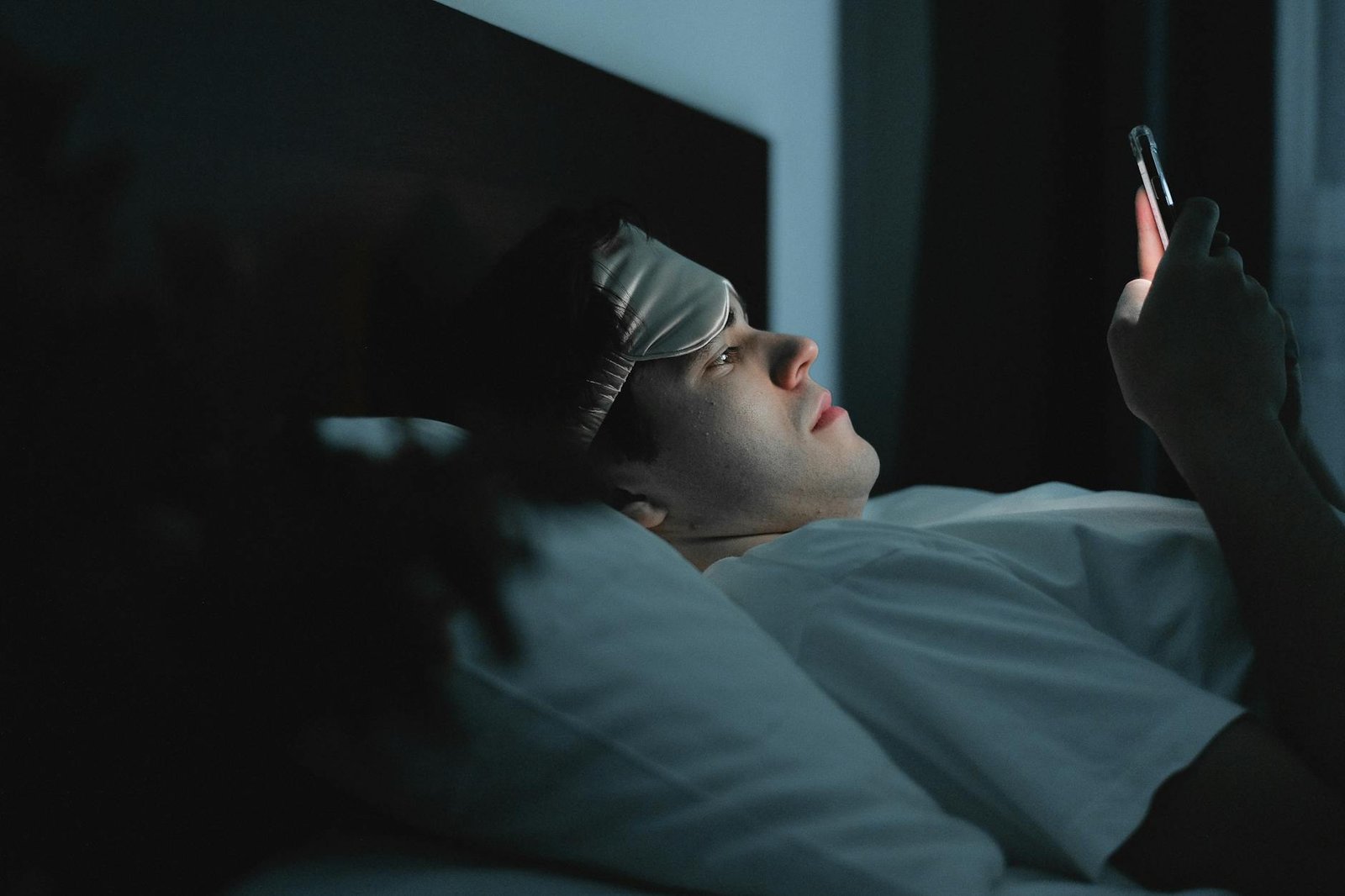 person lying awake in bed at night with soft blue light from a window looking frustrated and tired